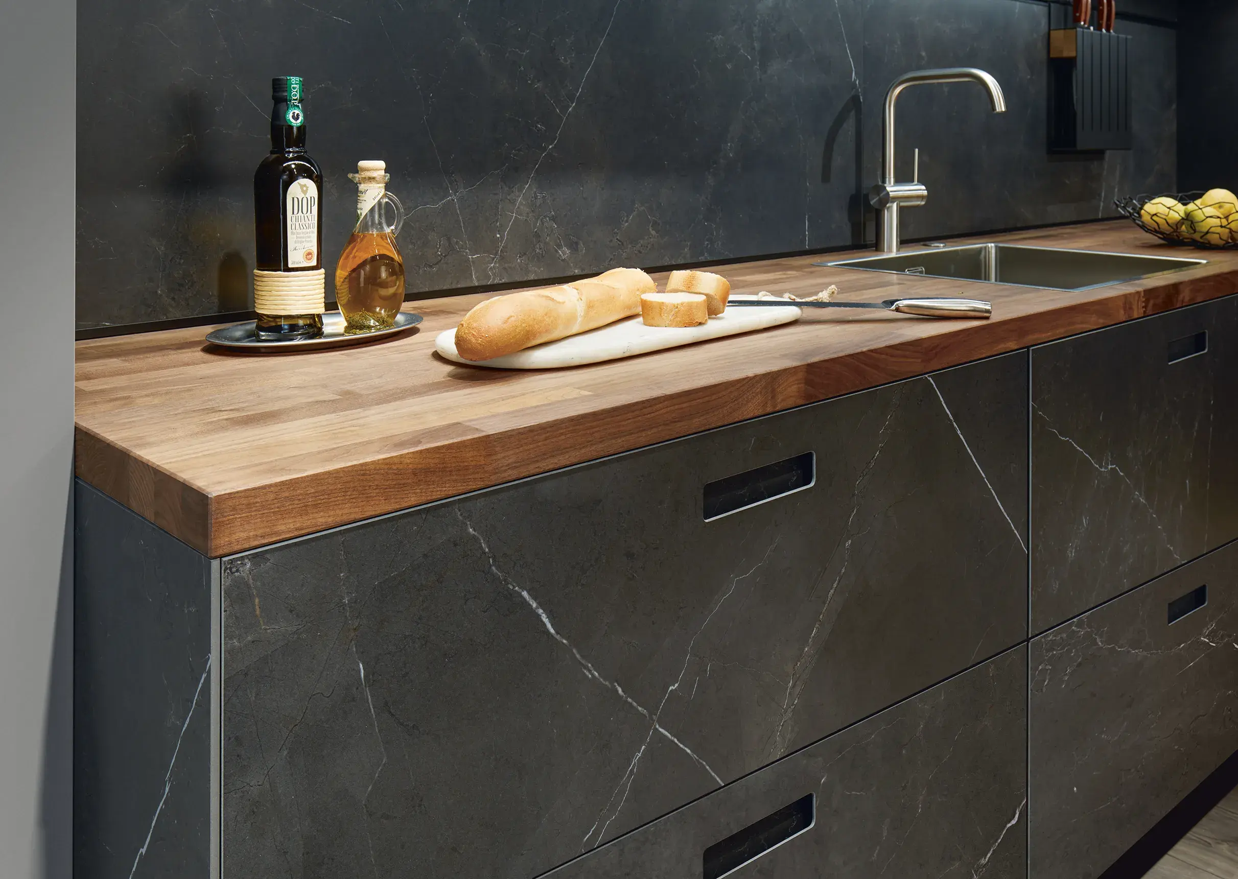 systemo Massivholzarbeitsplatte integrierte Edelstahlspüle Quarzstein-Küchenfronten und Nischenrückwand Holzbrett darauf mit Baguette und Brotmesser