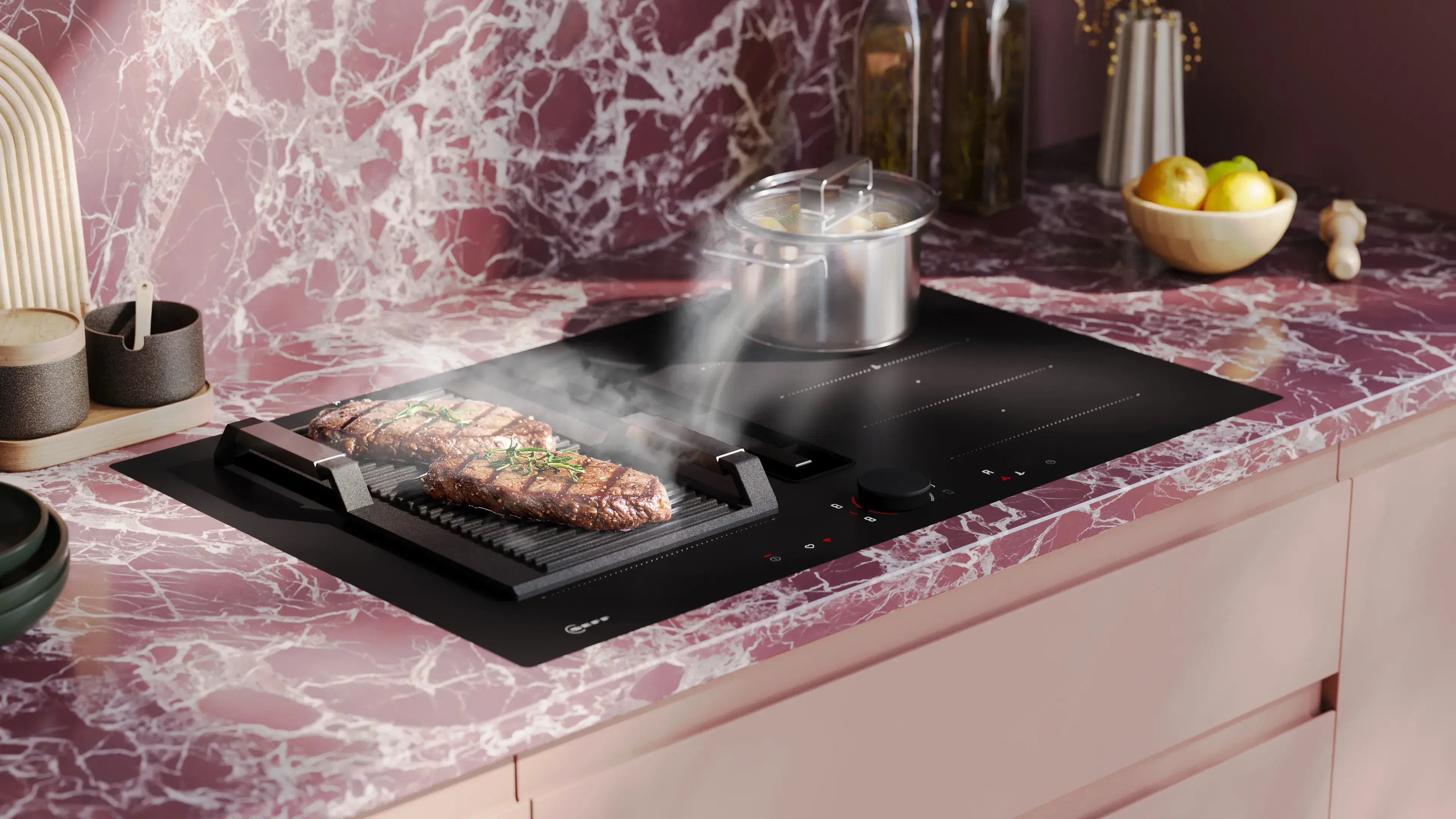 NEFF Collection Matt Black Design mattschwarzes Induktionskochfeld mit Teppan Grill-Aufsatz 2 Steaks auf rosa Arbeitsplatte Marmor-Optik Nischenrückwand gleich gestaltet